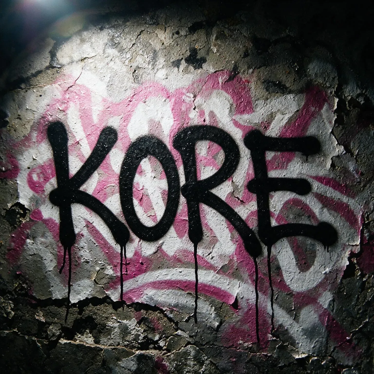A crumbling wall carrying a large tag in pink and black: KORE, the paint glowing against the ruined plaster.